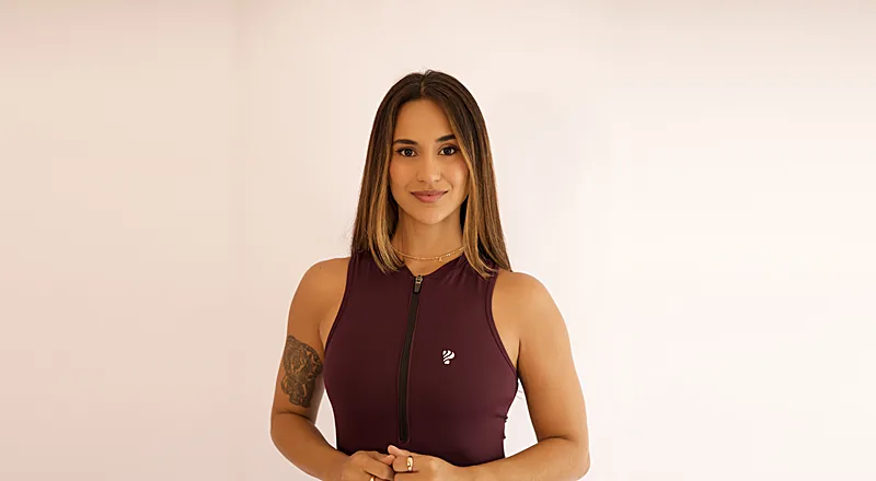 Ana Lacerda sorridente, vestindo top esportivo bordô, em retrato de estúdio.